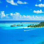 Aerial view of a luxurious tropical resort on a pristine island surrounded by azure waters and lush greenery.